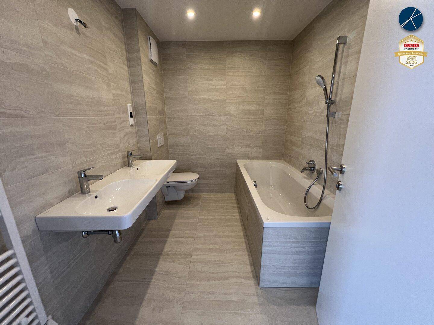 Geräumiges Badezimmer mit Badewanne, Wand-WC und Doppelwaschbecken.