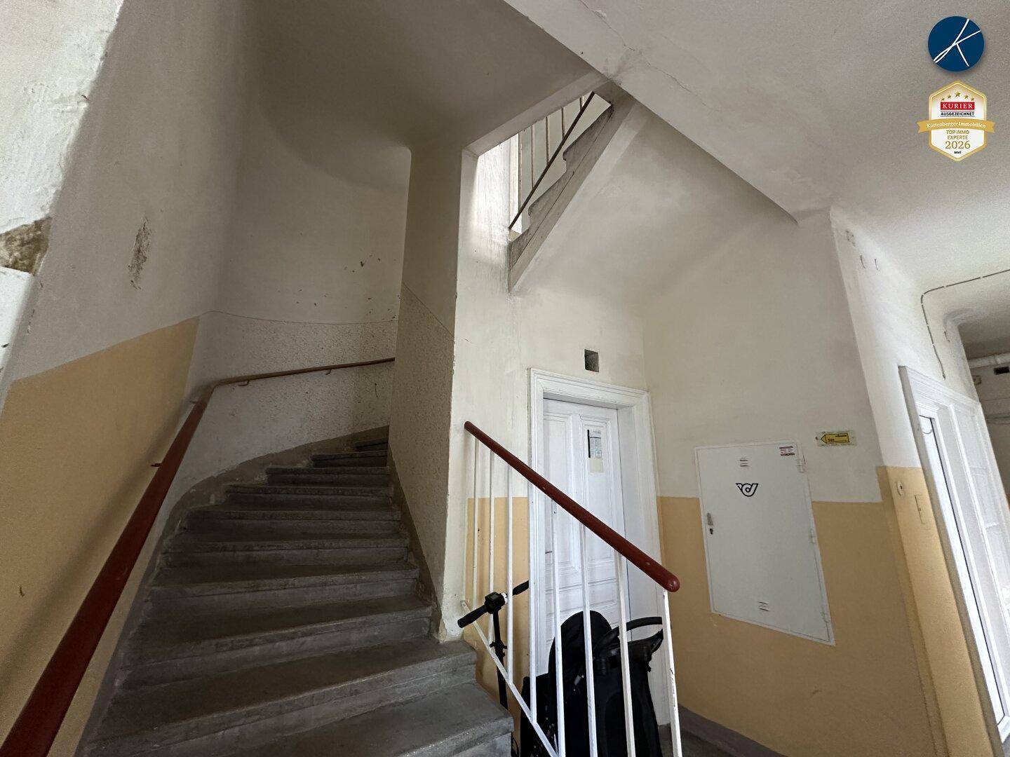 Helles Treppenhaus mit Steinstufen und Geländer in einem Altbau mit hohen Decken.