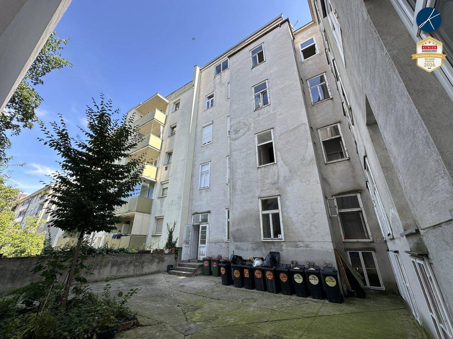Hinterhofbereich eines Altbaus mit Mülltonnen und Blick auf die Gebäuderückseite.