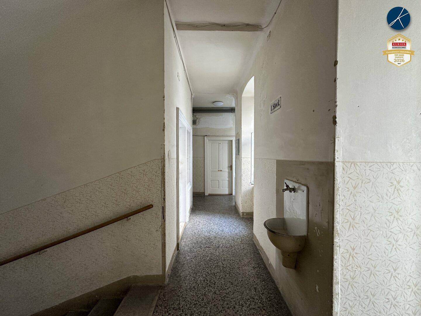 Langer Flur in einem Altbau mit Terrazzoboden und einem alten Waschbecken an der Wand.