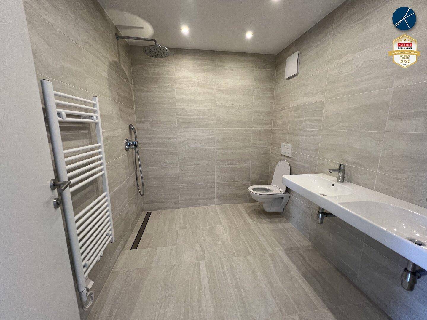 Modernes Badezimmer mit grauen Fliesen, ebenerdiger Dusche und wandhängendem WC.