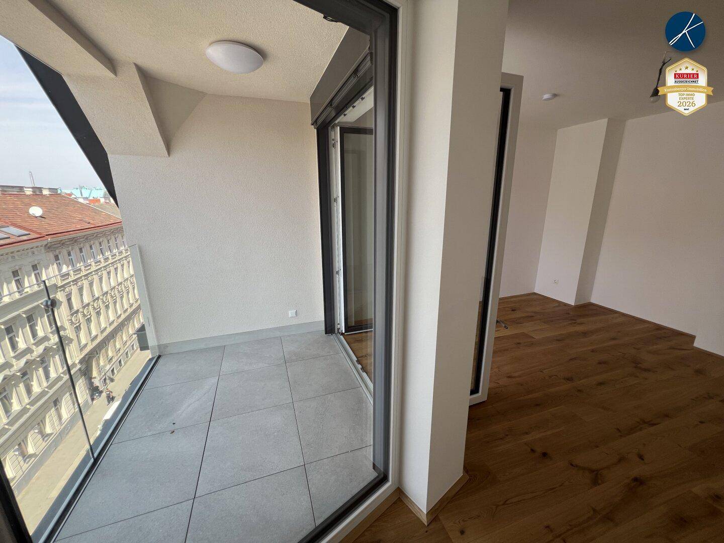 Innenraum mit Holzboden und direktem Zugang zu einem gefliesten Balkon mit Stadtblick.