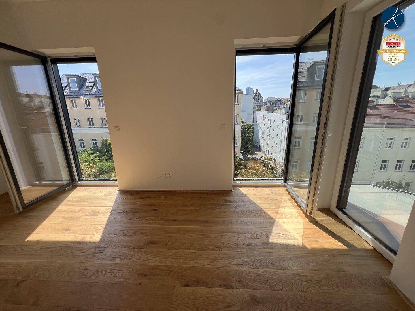 Lichtdurchfluteter Raum mit Holzboden und bodentiefen Fenstern, die einen Stadtblick bieten.