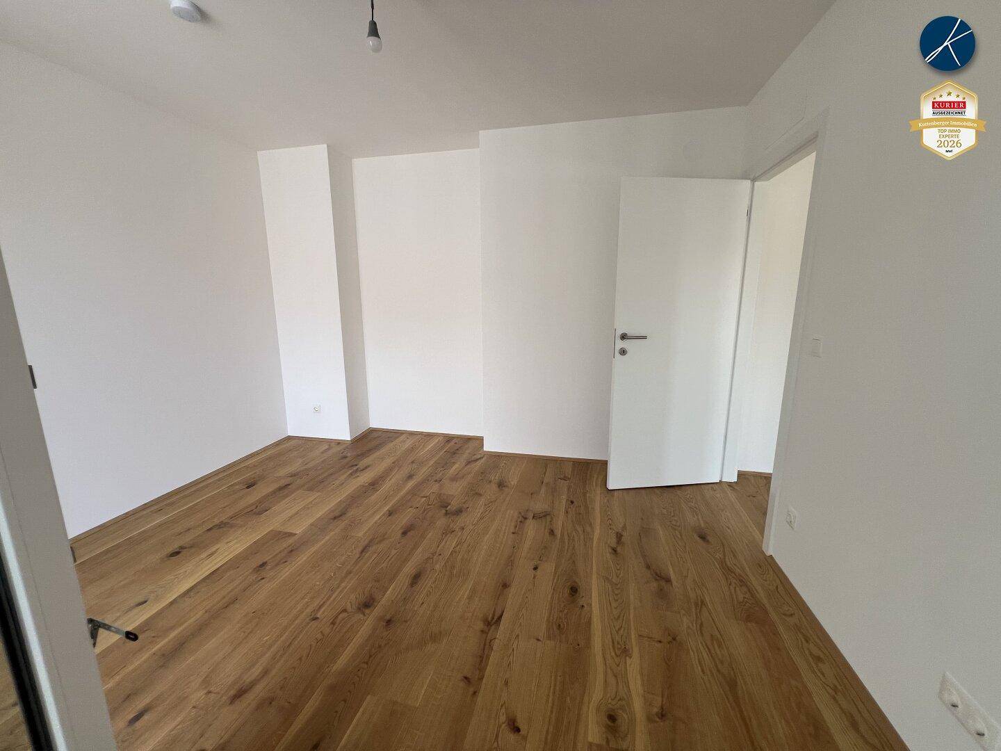 Helles, leeres Schlafzimmer mit Holzboden und weißen Wänden, bereit zur Einrichtung.