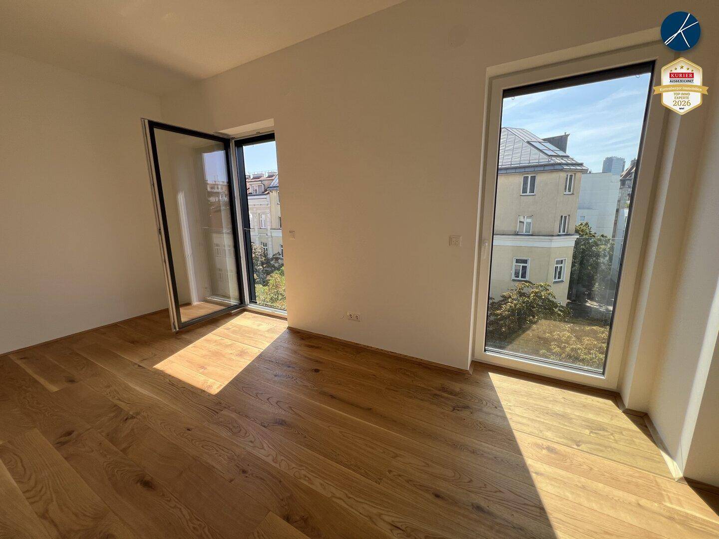 Heller Raum mit Holzboden und großen Fenstern, die viel Tageslicht hereinlassen.