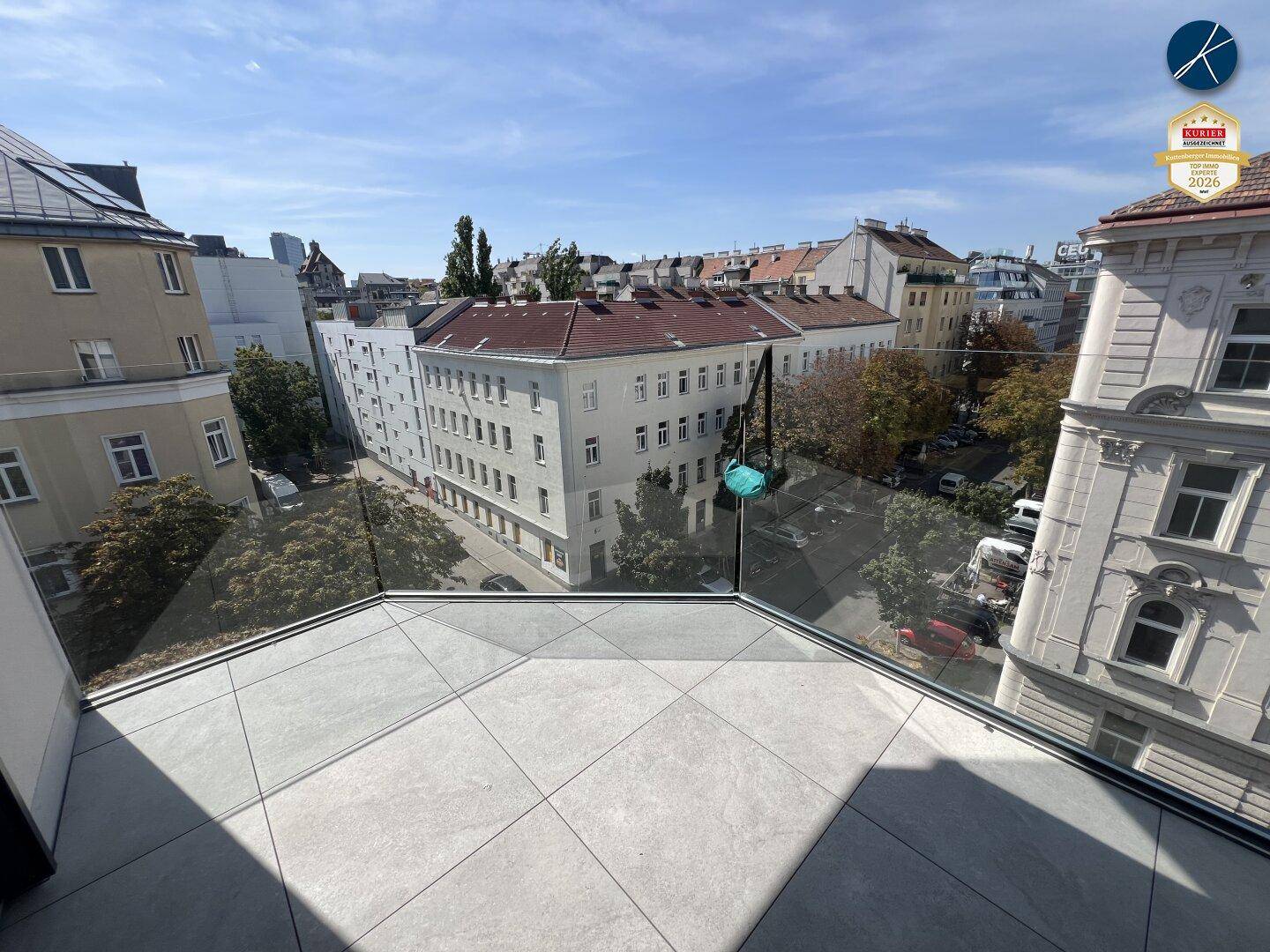 Großer Balkon mit Fliesenboden und Glasbrüstung, bietet einen Panoramablick über die Stadt.