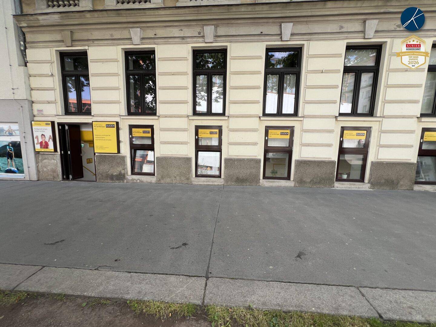 Historische Fassade eines Gebäudes mit mehreren Fenstern und Eingangsbereich auf Straßenniveau.