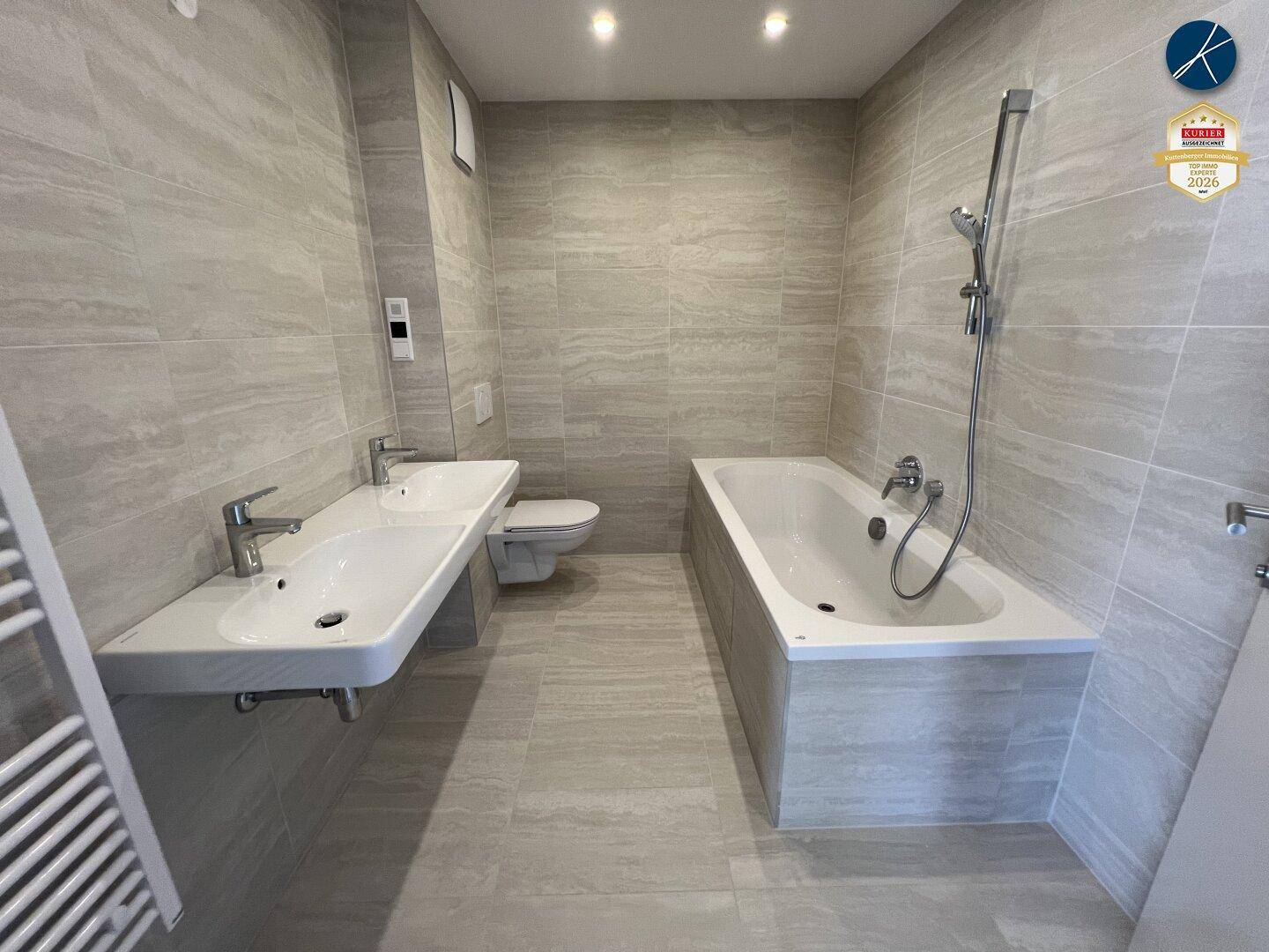 Modernes Badezimmer mit Doppelwaschbecken, Badewanne und hellen Fliesen.