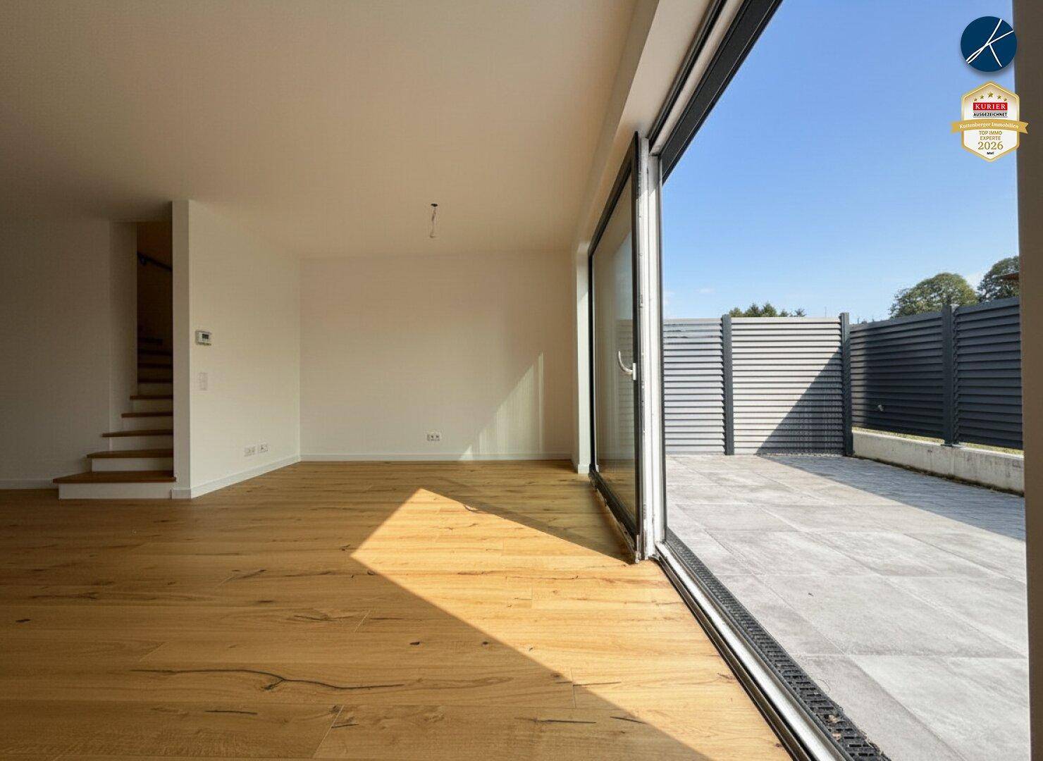 Geräumiges, unmöbliertes Wohnzimmer mit Holzboden und großen Schiebetüren zur Terrasse.