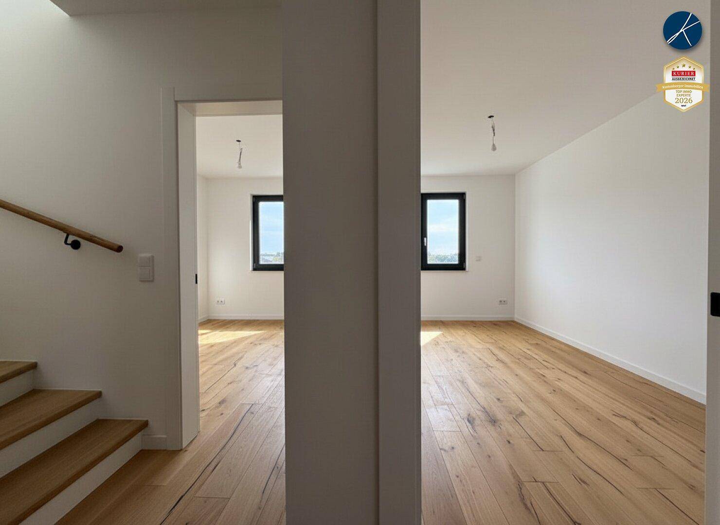Zwei helle, unmöblierte Zimmer mit Holzboden und Fenstern, getrennt durch eine Wand.