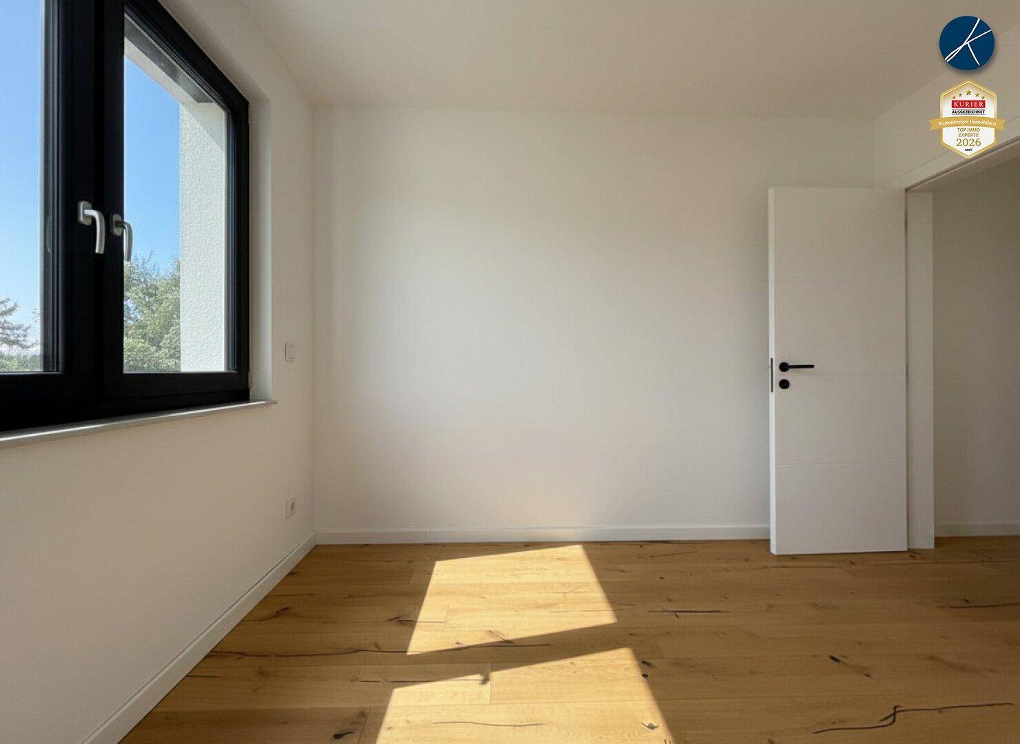 Helles Schlafzimmer mit Holzboden, weiß gestrichenen Wänden und großem Fenster.