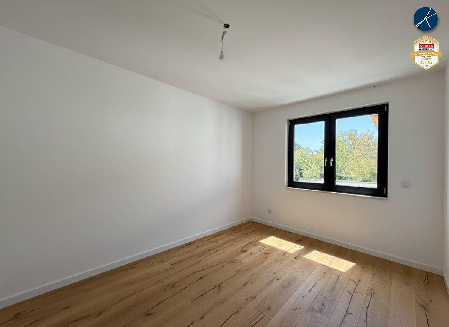 Helles Schlafzimmer mit Holzboden und Fenster, das viel Tageslicht hereinlässt.