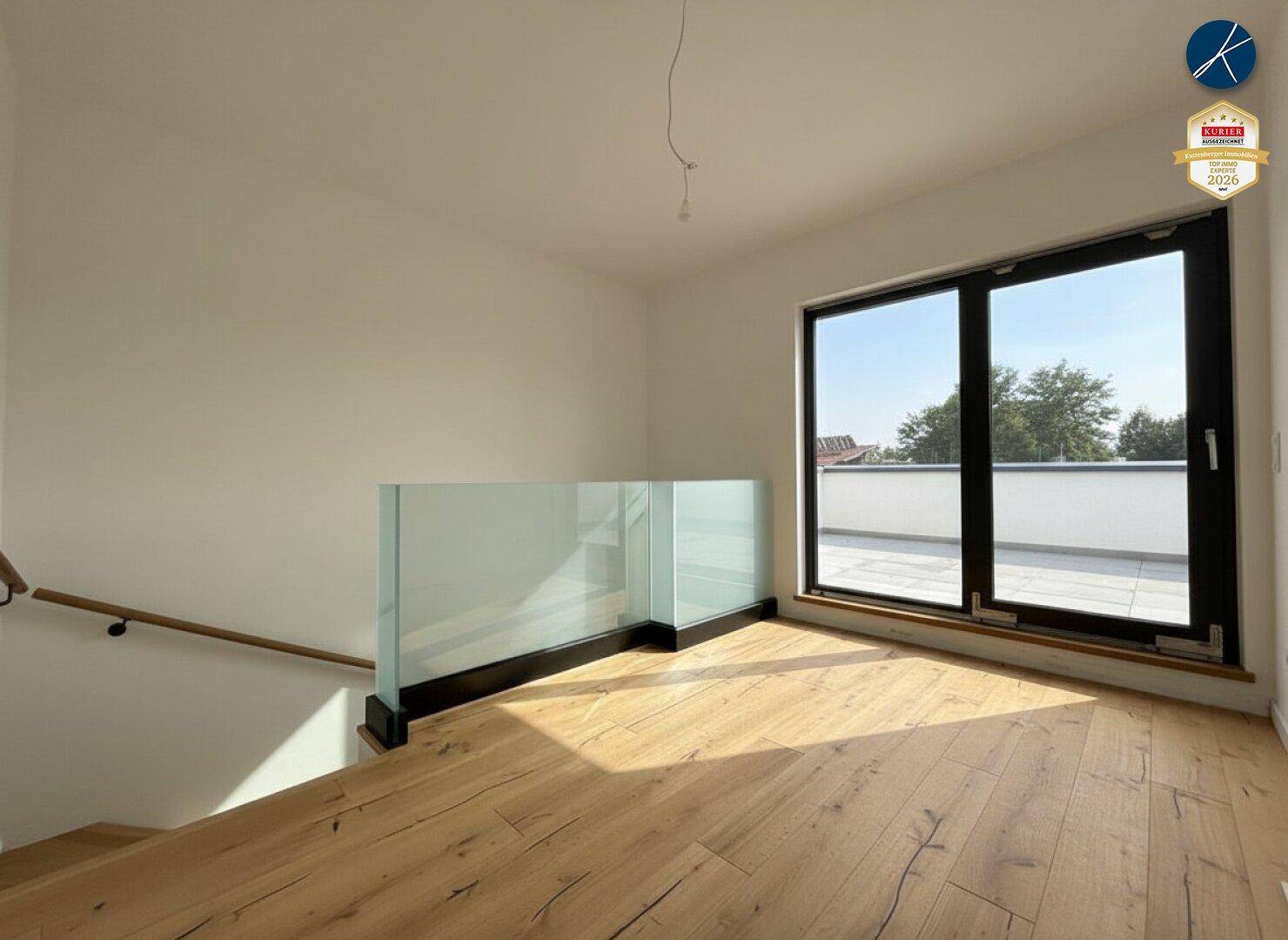 Heller offener Bereich mit Holzboden, Glasgeländer und Zugang zu einer großen Dachterrasse.