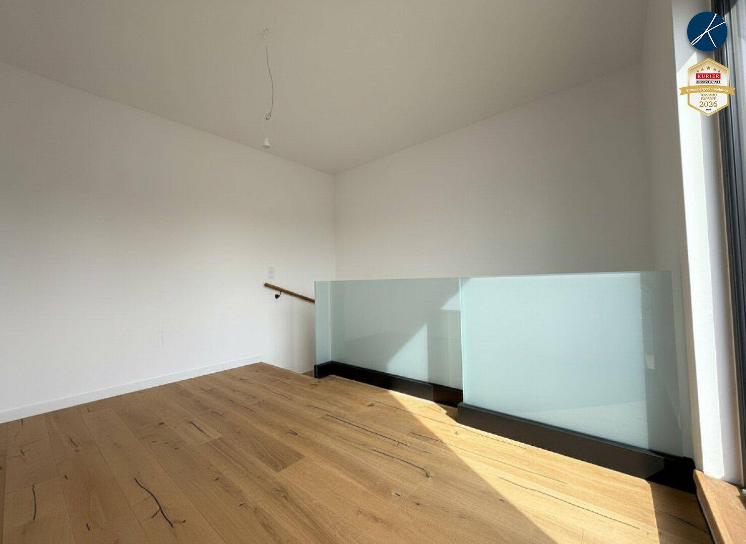 Offener Bereich mit Holzboden und modernem Glasgeländer, der viel natürliches Licht erhält.