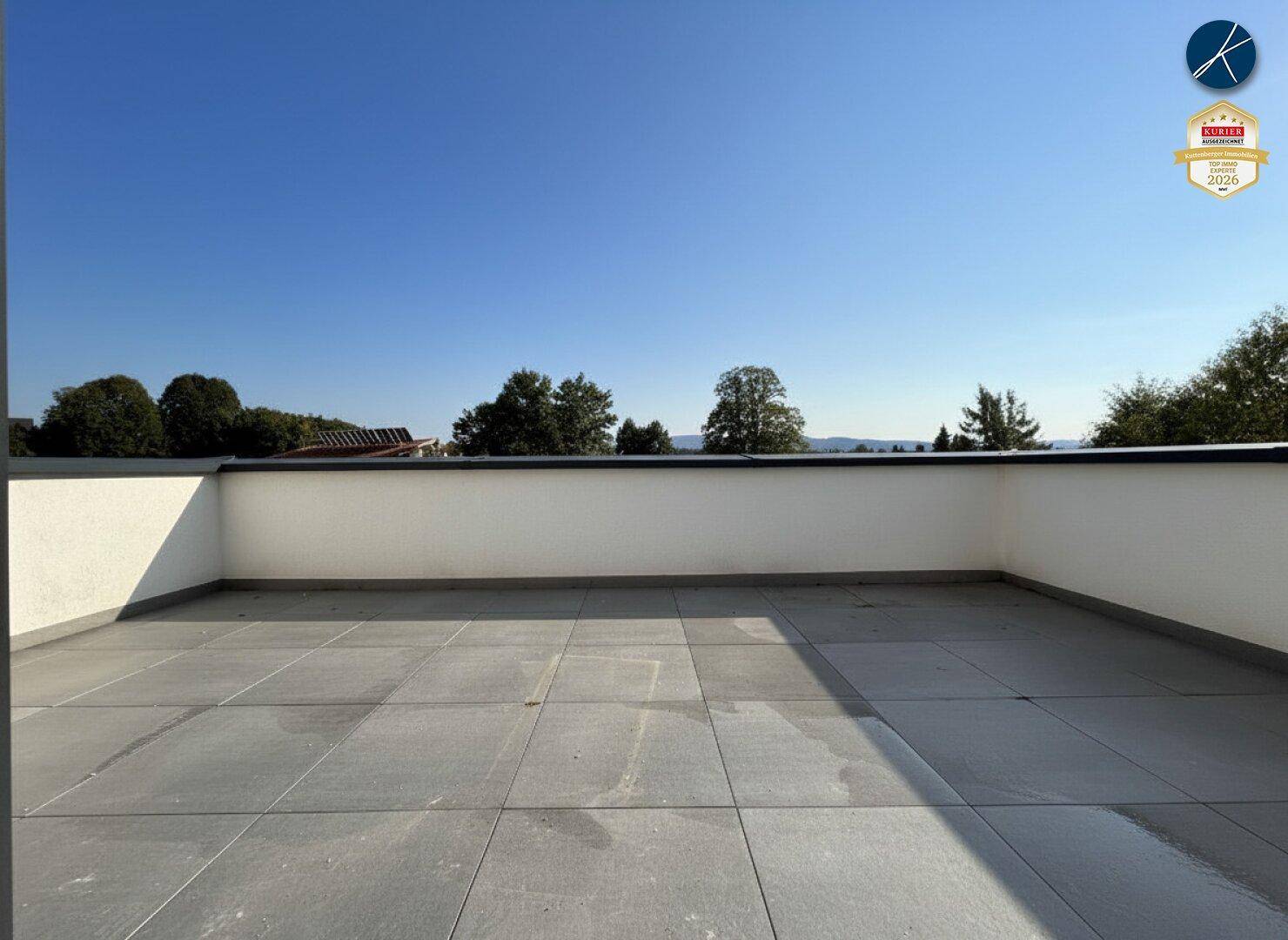 Weitläufige Dachterrasse mit Fliesenboden und hoher Brüstung, bietet viel Platz im Freien.