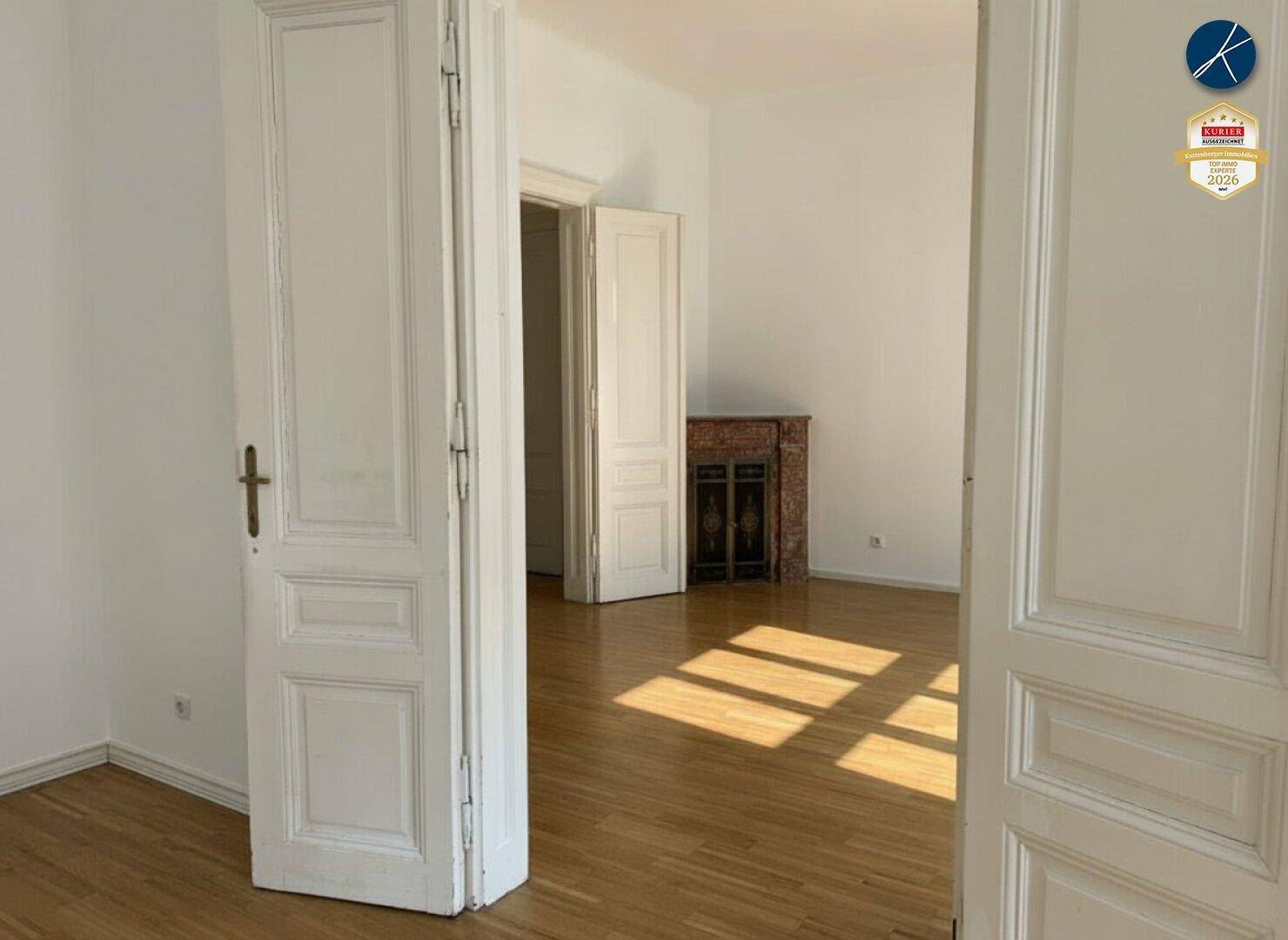 Helles Zimmer mit Parkettboden und einem dekorativen Kamin, das viel Tageslicht empfängt.