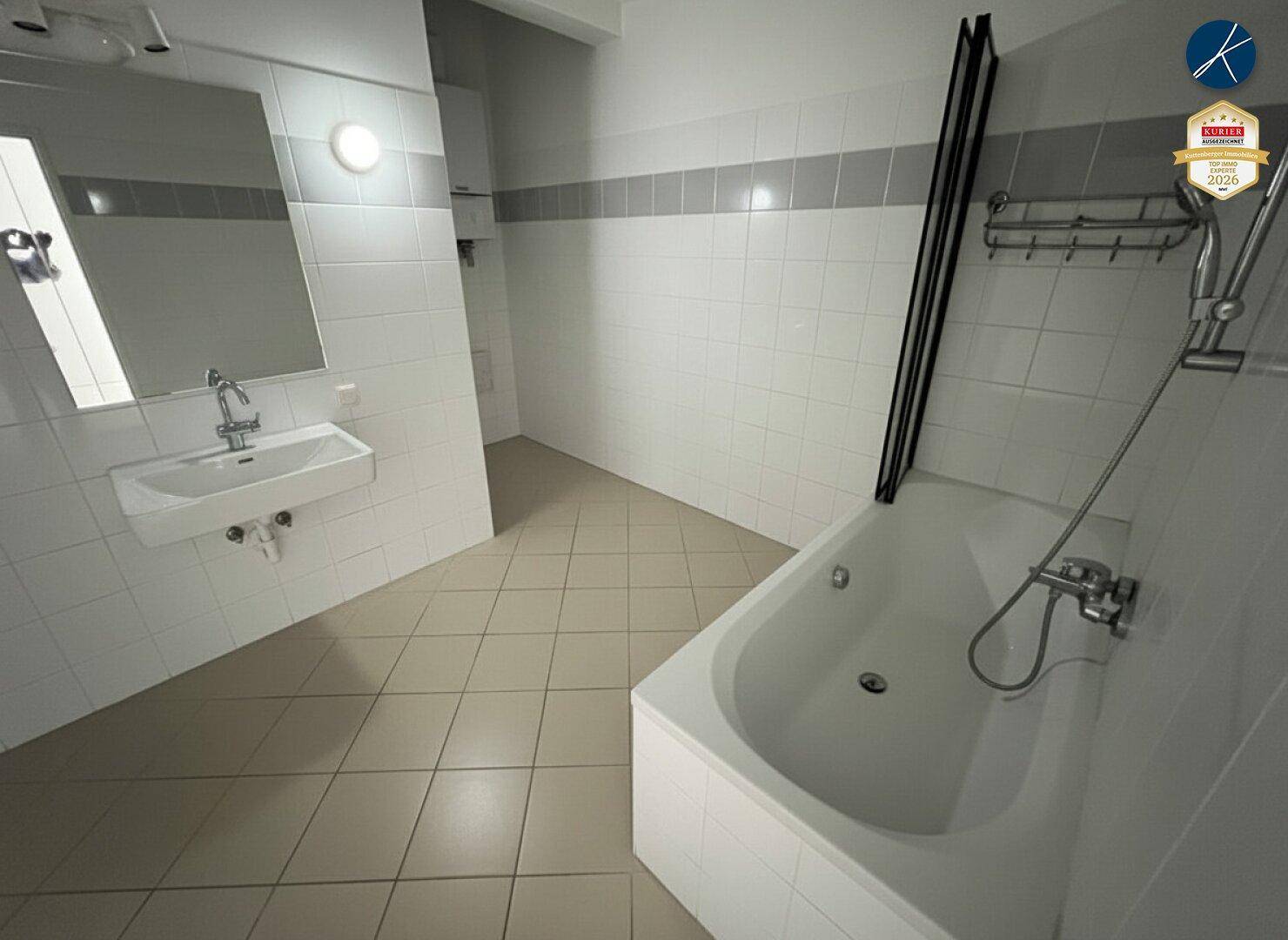Badezimmer mit Badewanne, Waschbecken und hellen Fliesen an Wänden und Boden.