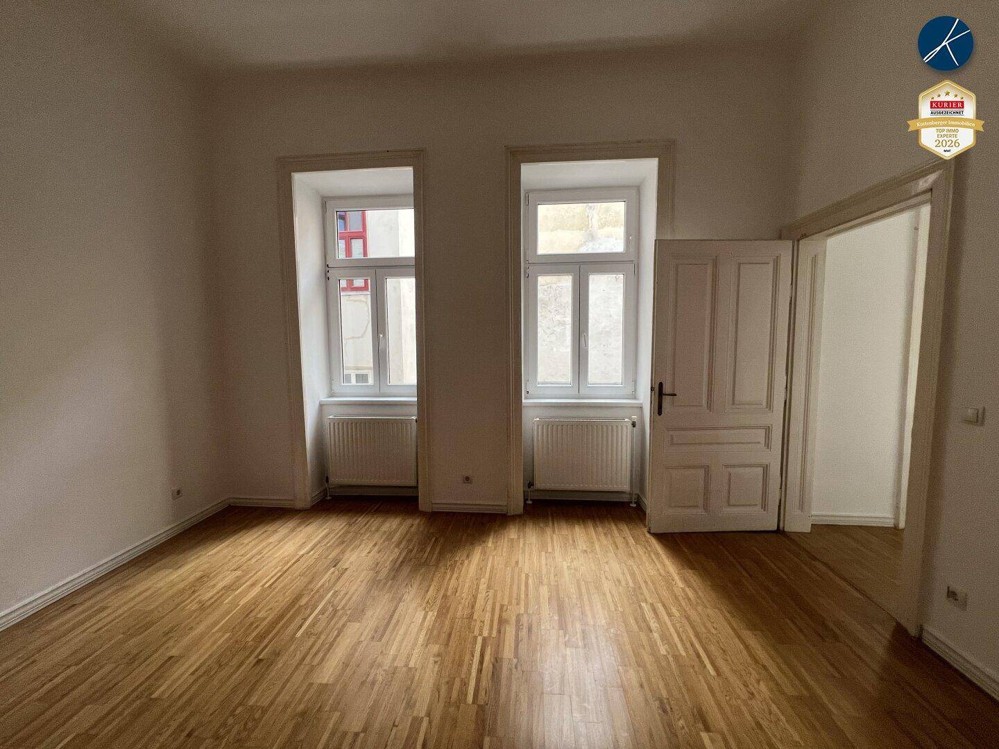 Geräumiges Zimmer mit Parkettboden und zwei Fenstern, die für natürliche Beleuchtung sorgen.