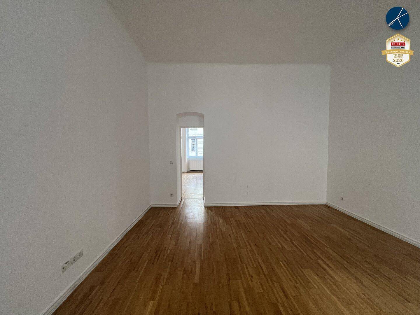 Leeres Zimmer mit Parkettboden und einem Durchgang zu einem weiteren Raum.