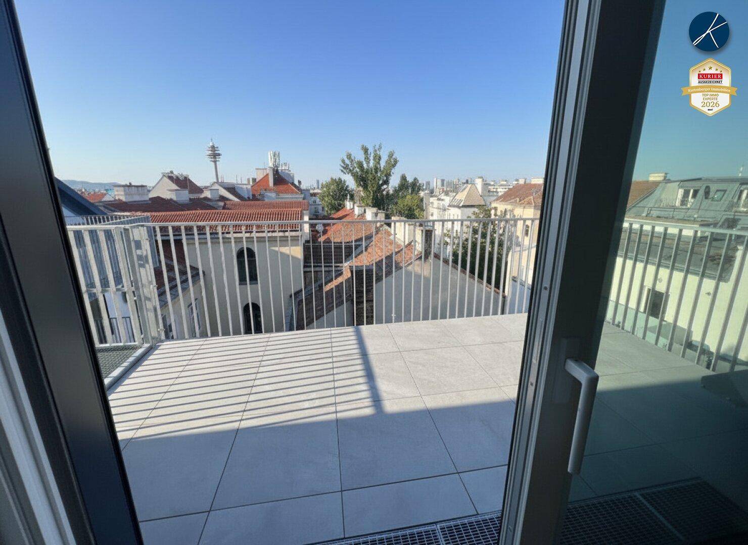 Blick von innen auf eine sonnige Terrasse mit Fliesenboden und weitem Stadtpanorama.