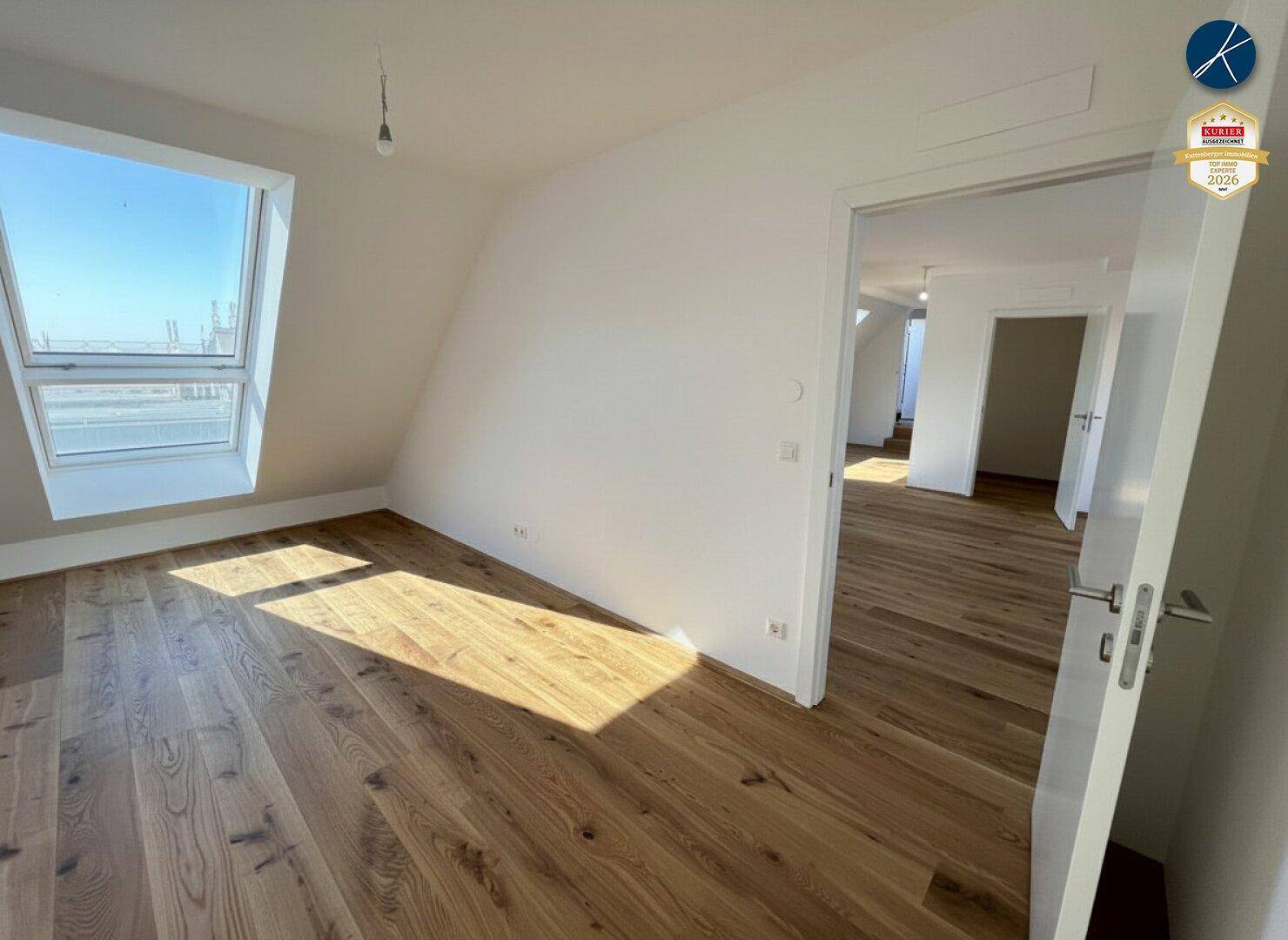 Lichtdurchfluteter Raum mit Holzparkett und großem Dachfenster unter einer schrägen Decke.