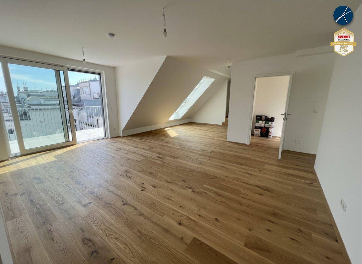 Heller Raum mit Holzparkett, Zugang zum Balkon und schrägen Decken mit Dachfenster.
