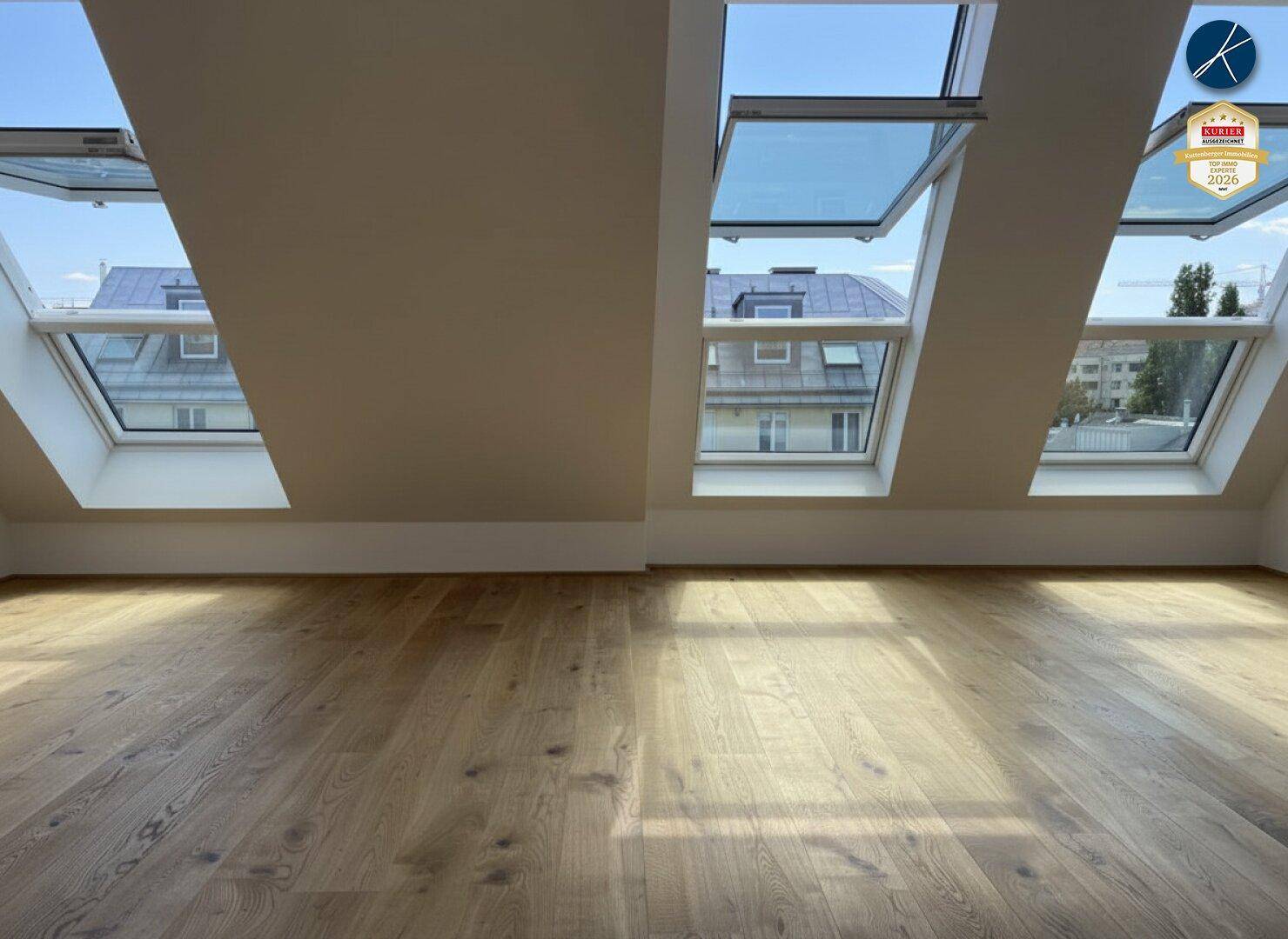 Lichtdurchfluteter Raum im Dachgeschoss mit Holzboden und mehreren großen Dachfenstern.