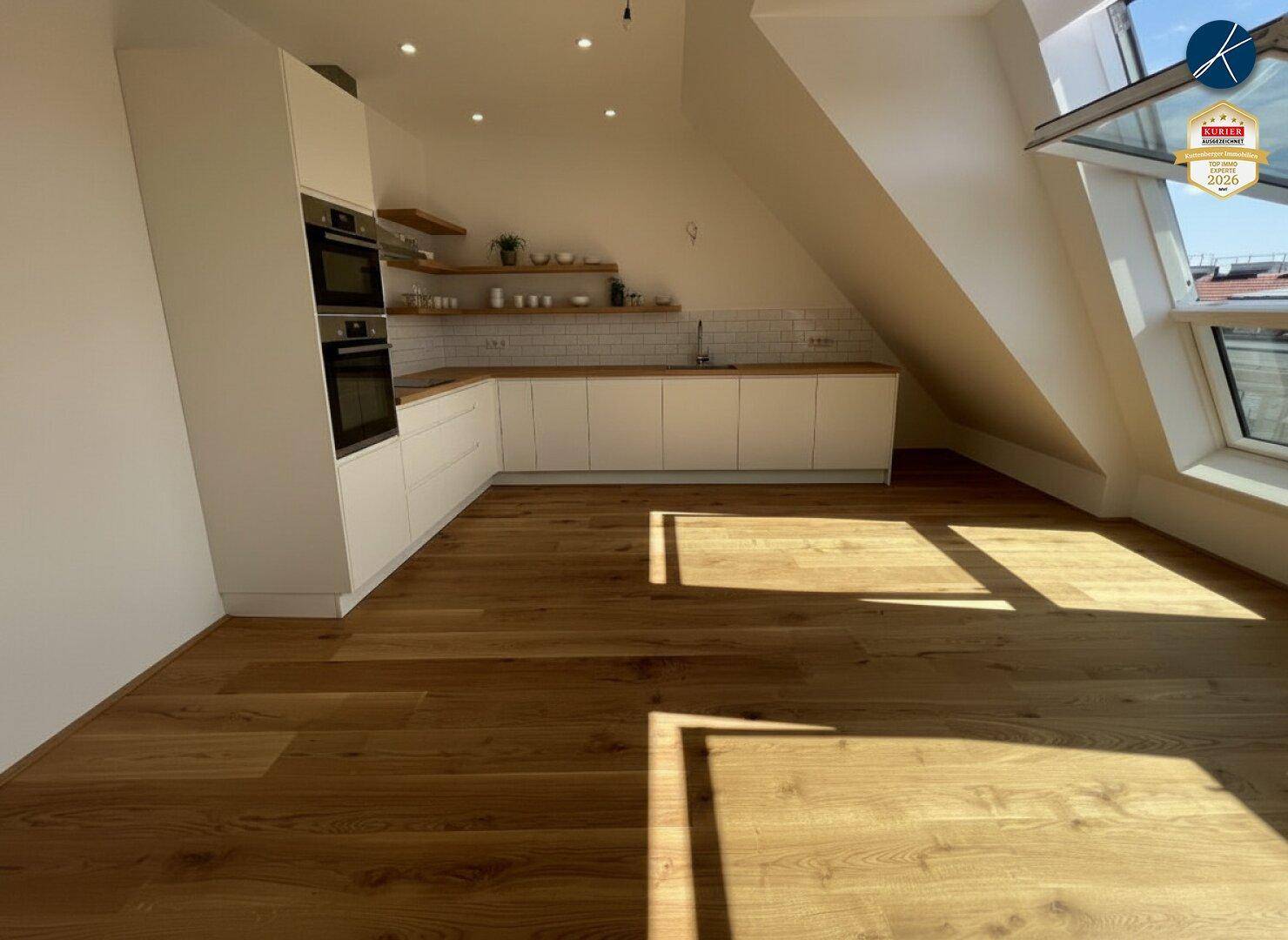 Helle Küche im Dachgeschoss mit Holzboden, Dachfenstern und modernen Einbauschränken.