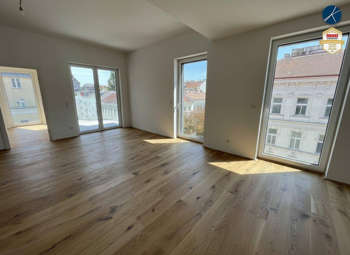 Geräumiger, heller Raum mit Holzboden und Zugang zu einem Balkon oder einer Terrasse.