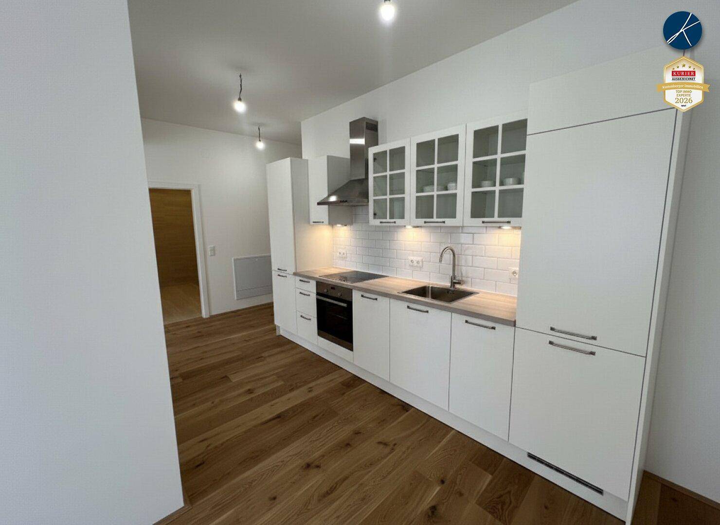 Moderne Einbauküche mit weißen Schränken, Holztheke und integrierten Geräten.