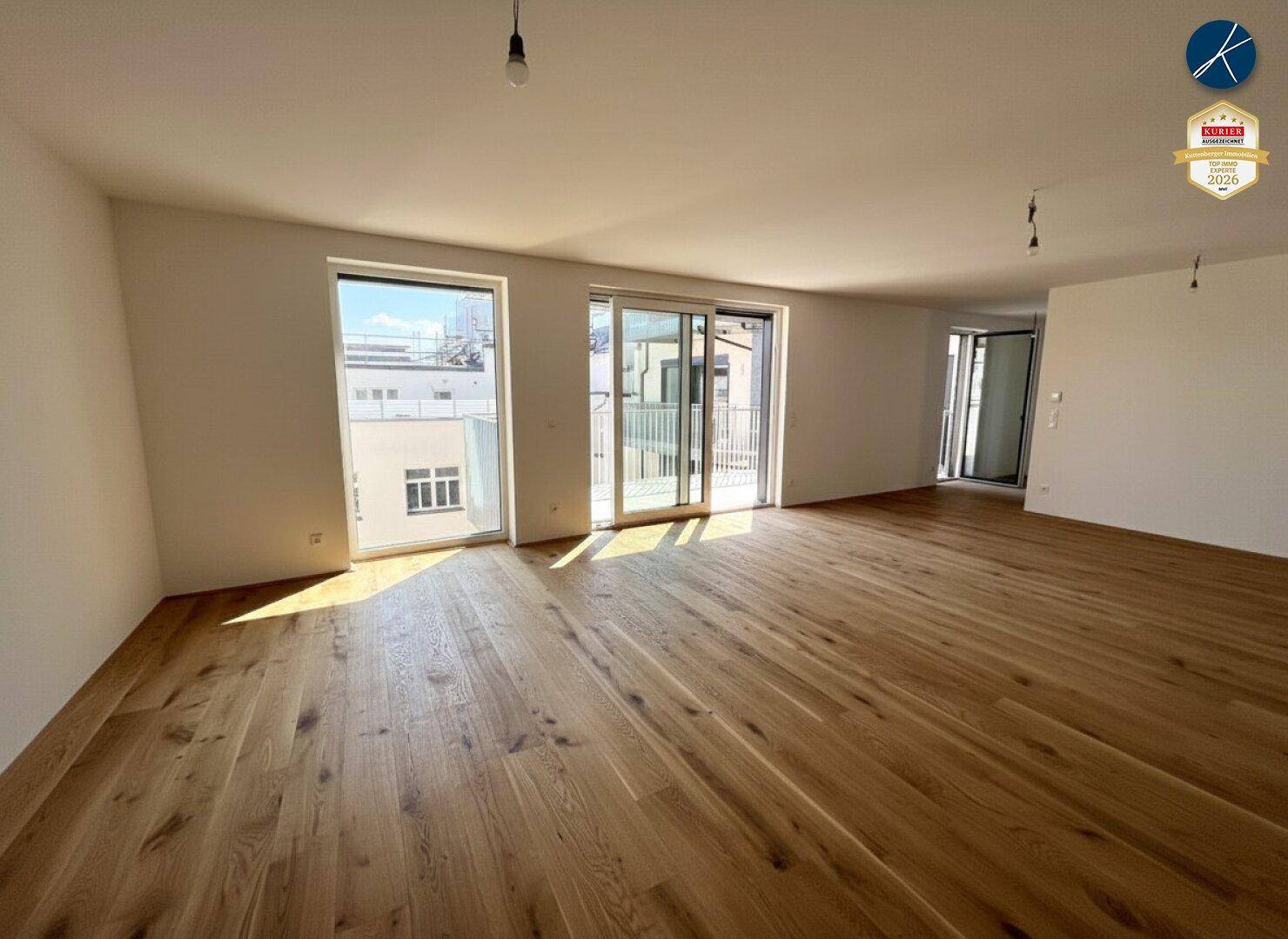 Lichtdurchfluteter Wohnbereich mit Holzboden und Schiebetüren, die zum Balkon führen.