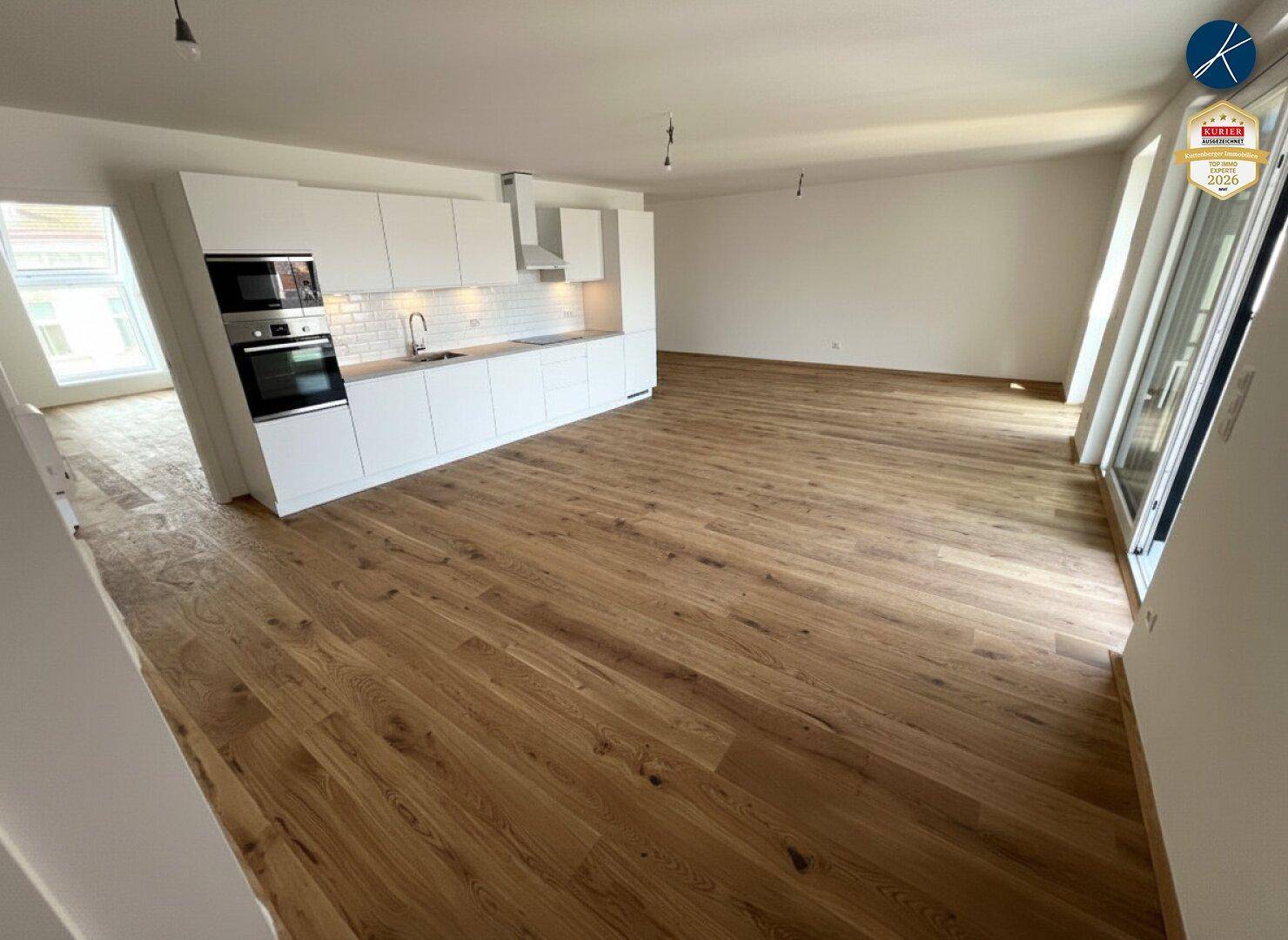 Moderne, offene Küche mit weißen Schränken und Holzboden in einem hellen Wohnbereich.