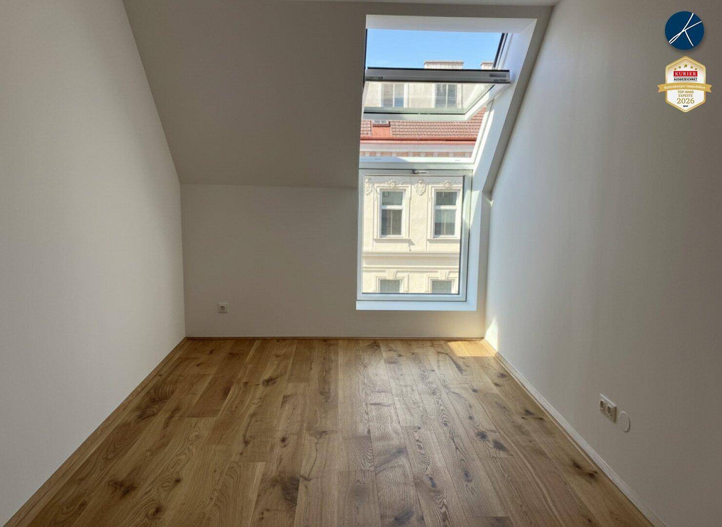 Dachzimmer mit Holzboden und großem Dachfenster, das einen Blick nach draußen bietet.