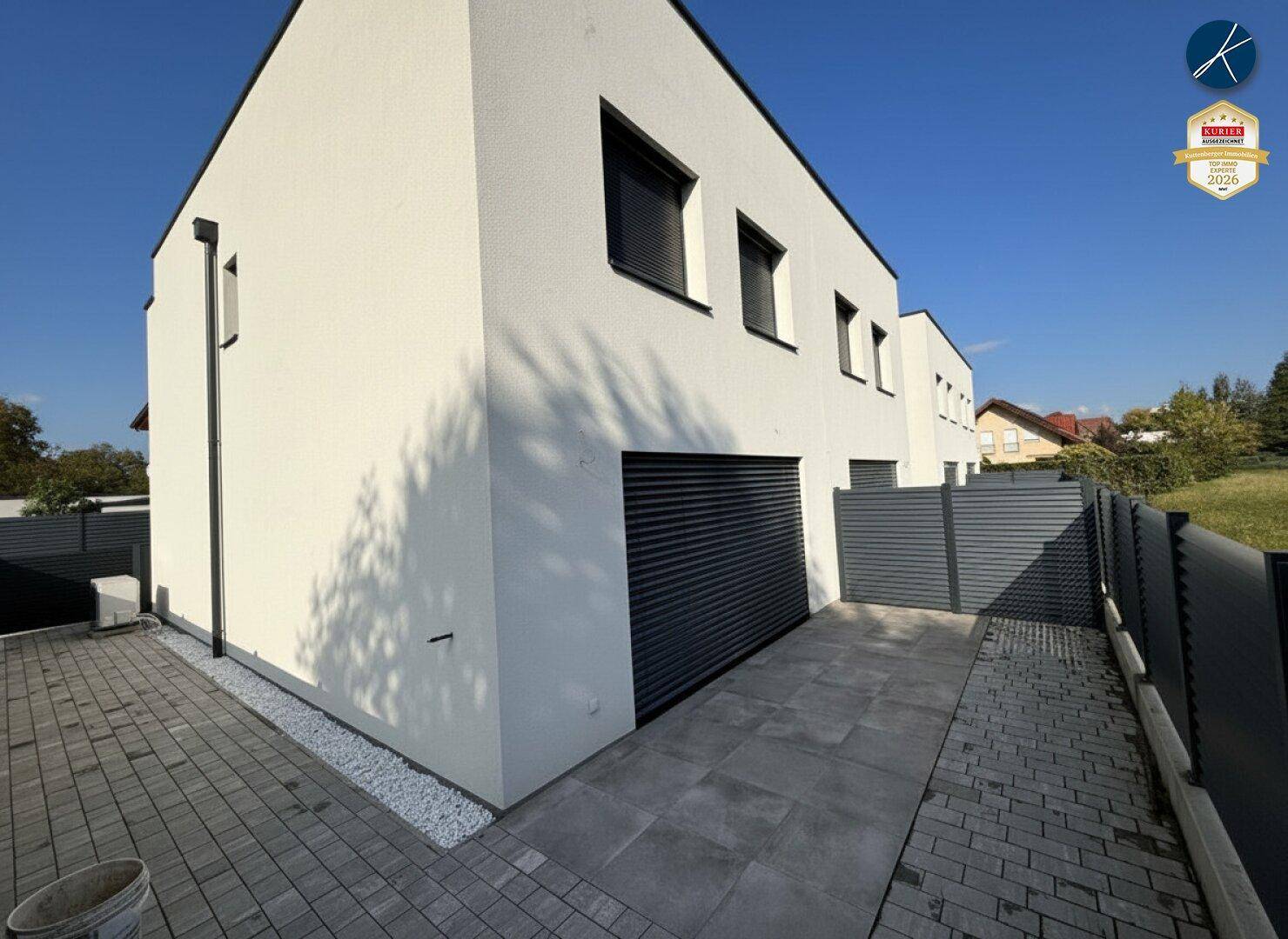 Seitenansicht eines modernen Neubaus mit weißer Fassade und Garagentor.