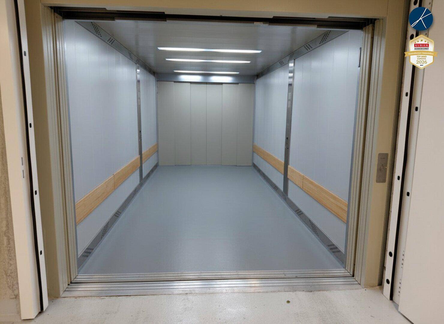 Geräumiger Lastenaufzug mit grauen Wänden und Holzbalken, ideal für größere Transporte.