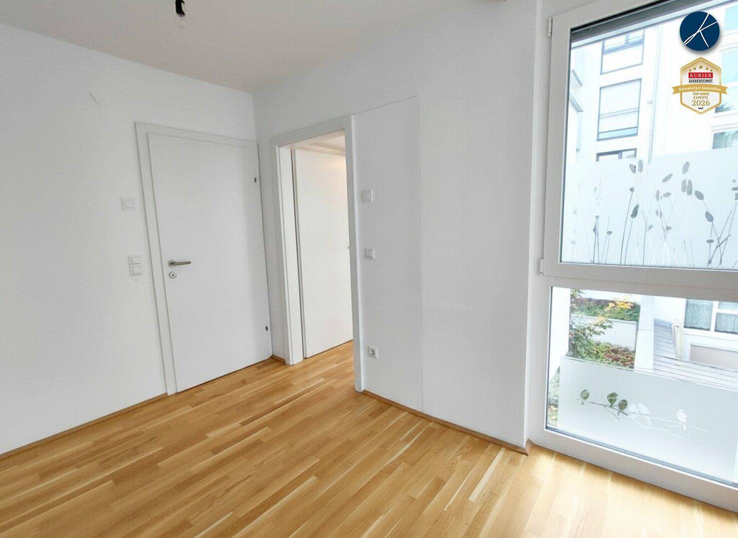 Heller Raum mit Holzparkettboden, weiß gestrichenen Wänden und großen Fenstern mit Sichtschutzfolie.