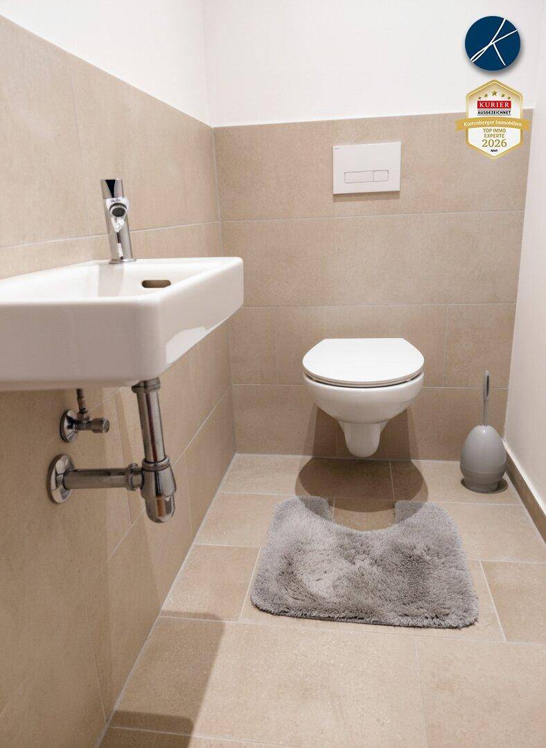 Helles Gäste-WC mit beigefarbenen Fliesen, wandhängendem WC und kleinem Waschbecken.