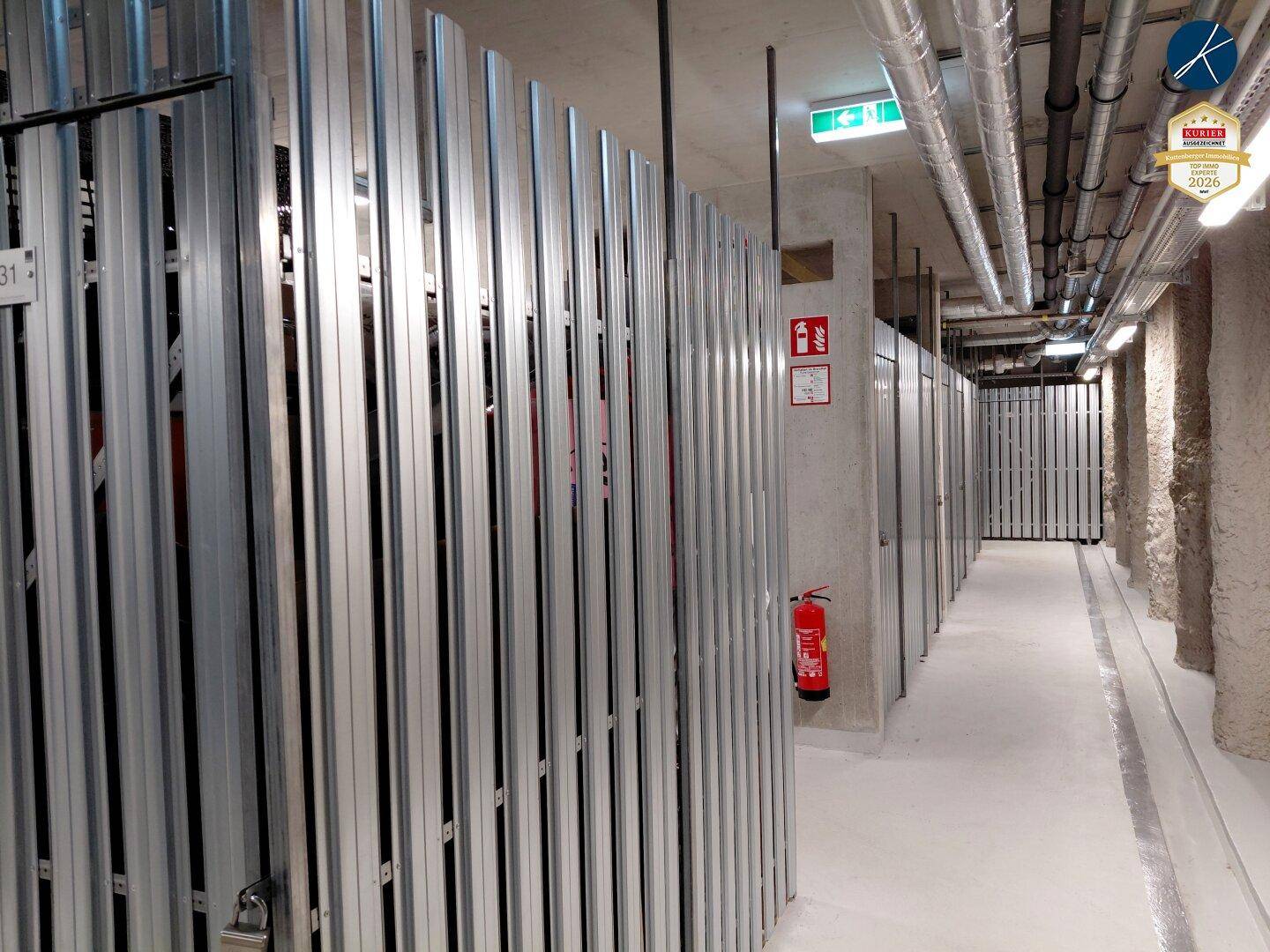 Kellerabteile mit Metallgittern und Betonwänden, gut beleuchtet und organisiert.