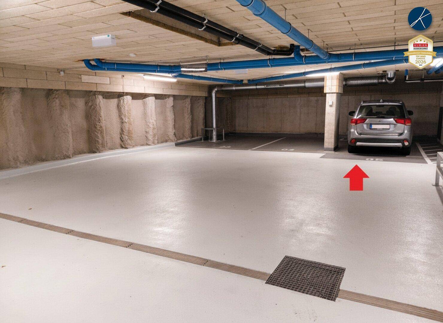 Tiefgarage mit markierten Stellplätzen, blauen Rohren an der Decke und einem geparkten Auto.
