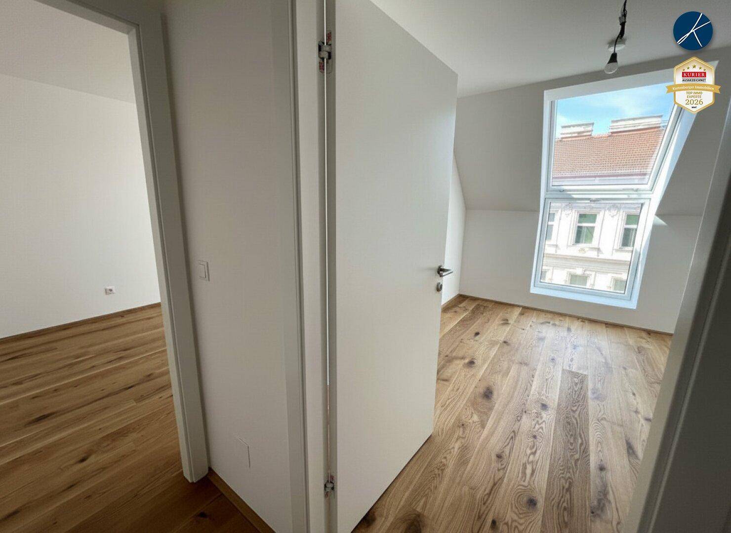 Helles Zimmer mit Dachschrägen, Holzboden und einem großen Dachfenster.