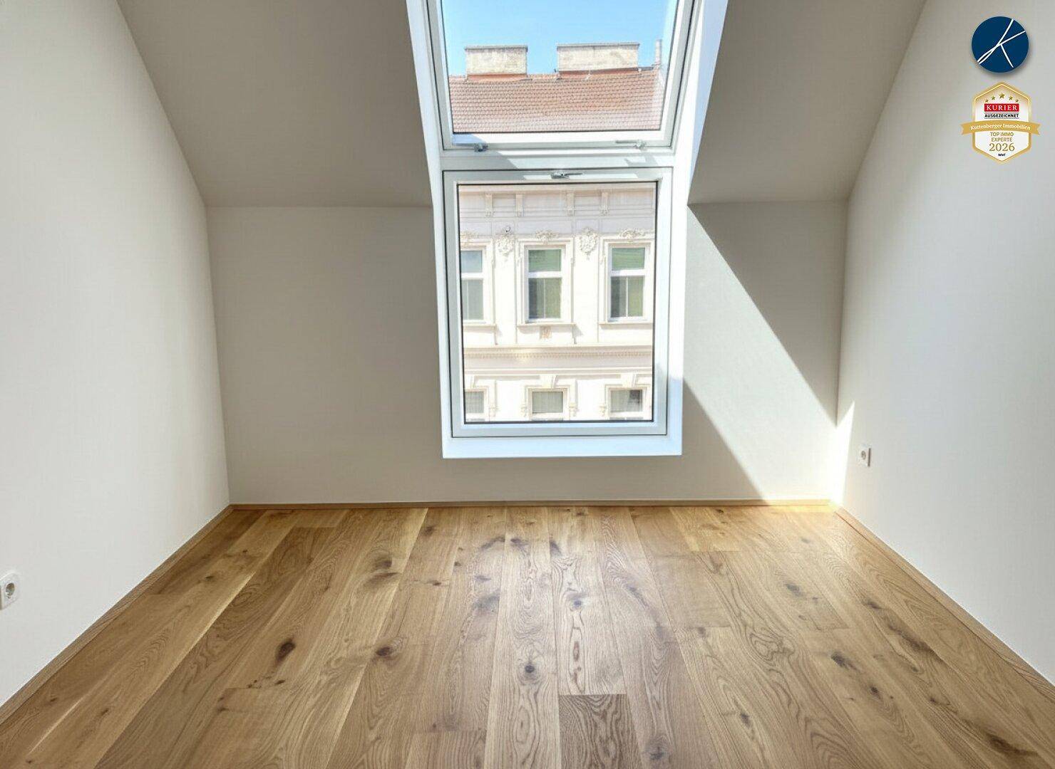 Dachzimmer mit schrägem Dachfenster, das viel Tageslicht hereinlässt und Stadtblick bietet.