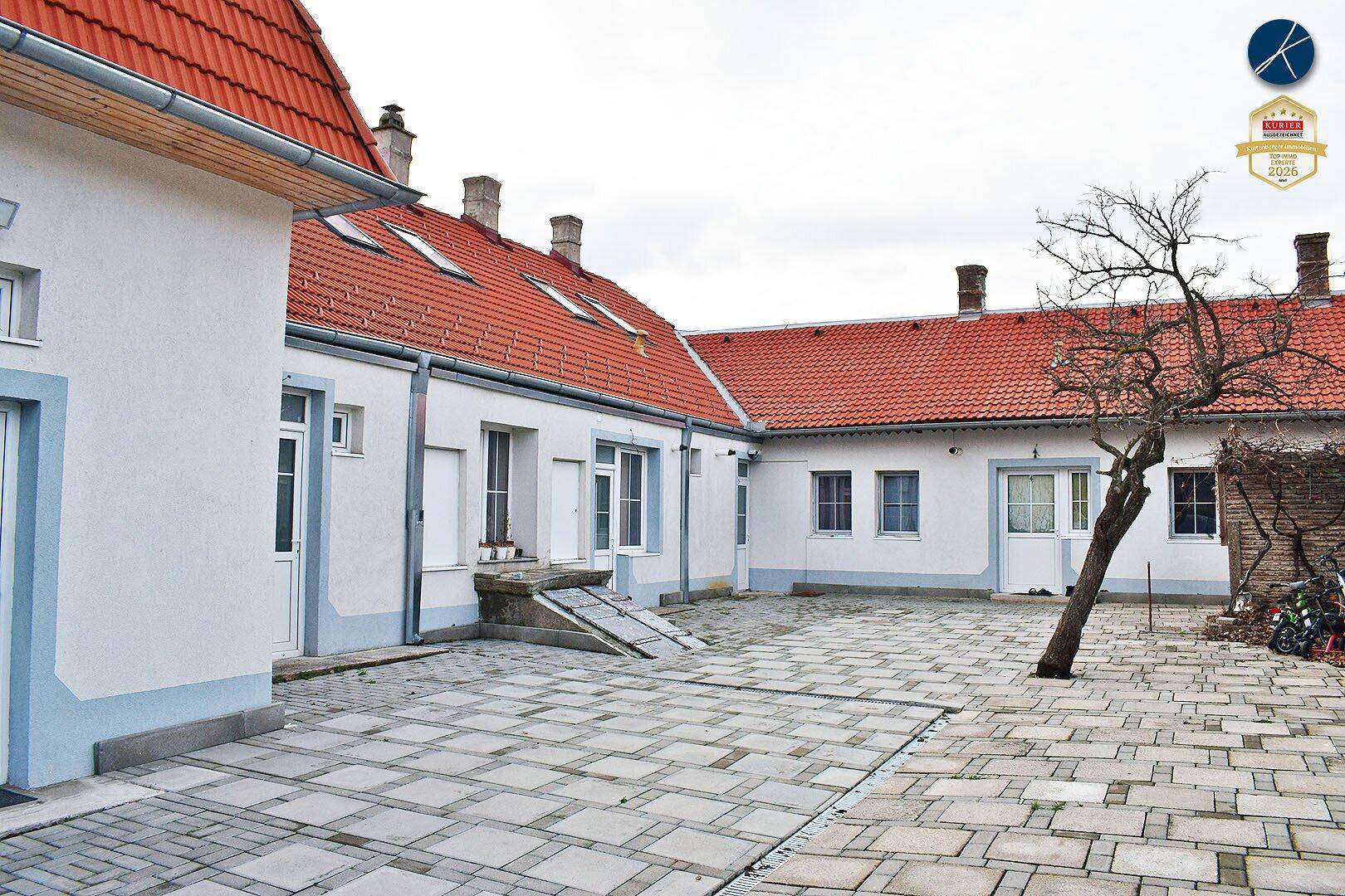 Großer gepflasterter Innenhof mit traditionellen Gebäuden und einem kahlen Baum.