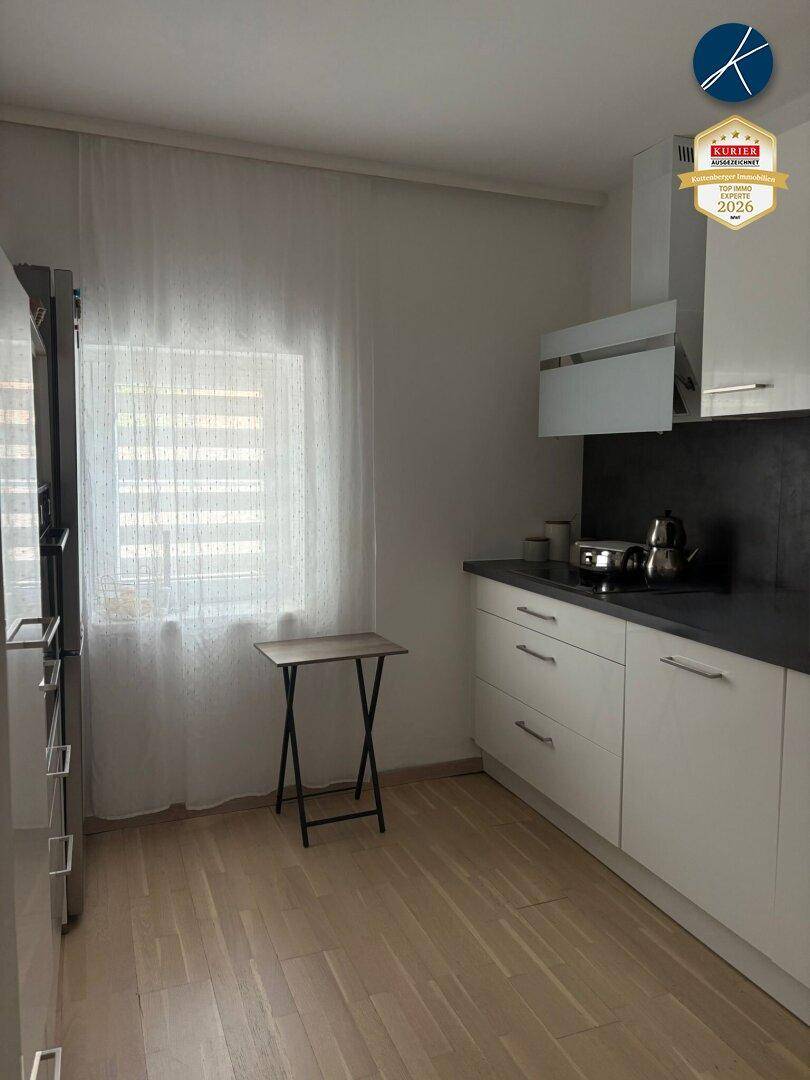 Funktionale Küche mit weißen Schränken, dunkler Arbeitsplatte und Fenster.