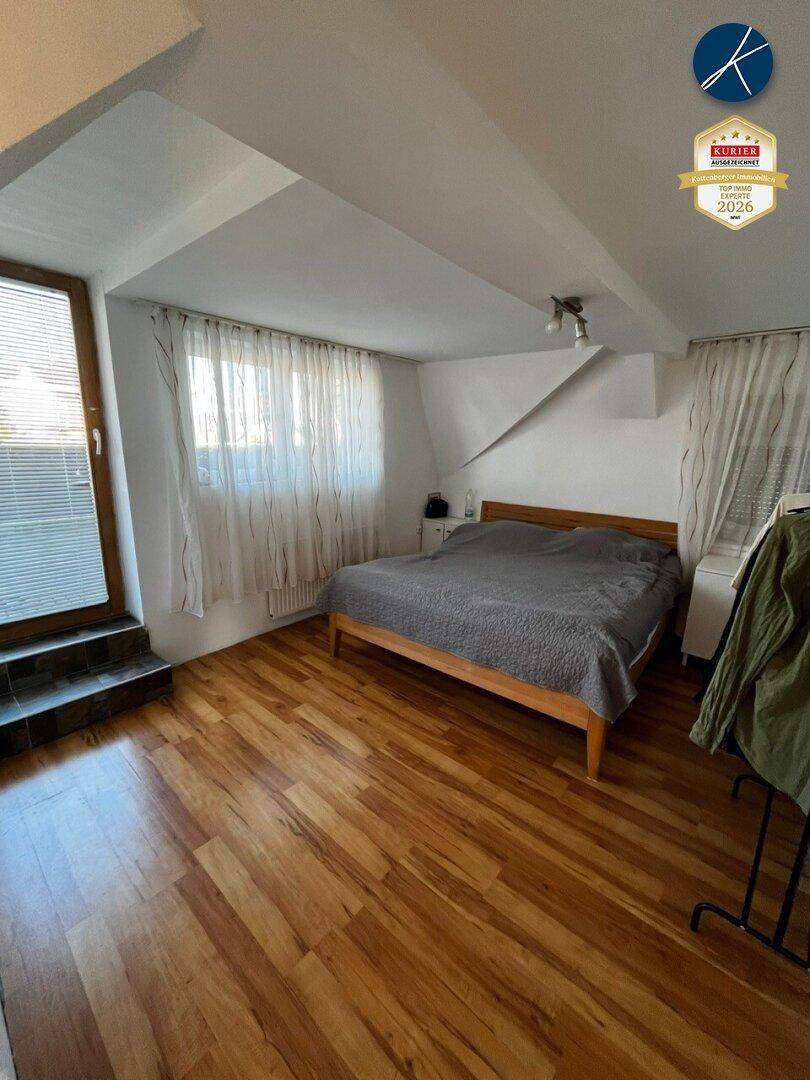 Schlafzimmer mit Holzboden, Doppelbett und Zugang zu einem kleinen Balkon oder Austritt.