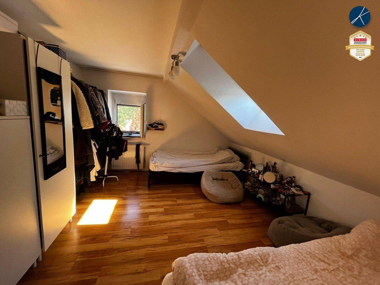 Dachgeschosszimmer mit Holzboden, Kleiderschrank und Dachfenster für natürliches Licht.