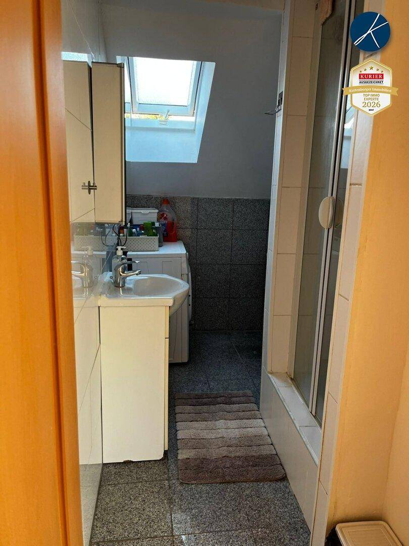 Badezimmer mit Dusche, Waschbecken, Waschmaschine und Dachfenster.