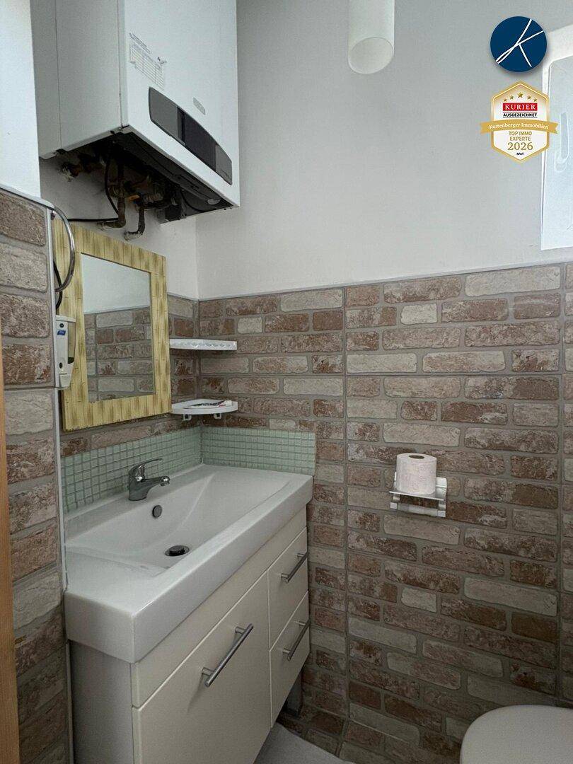 Kleines WC mit Waschbecken, Toilette und Wandfliesen im Ziegelmuster.