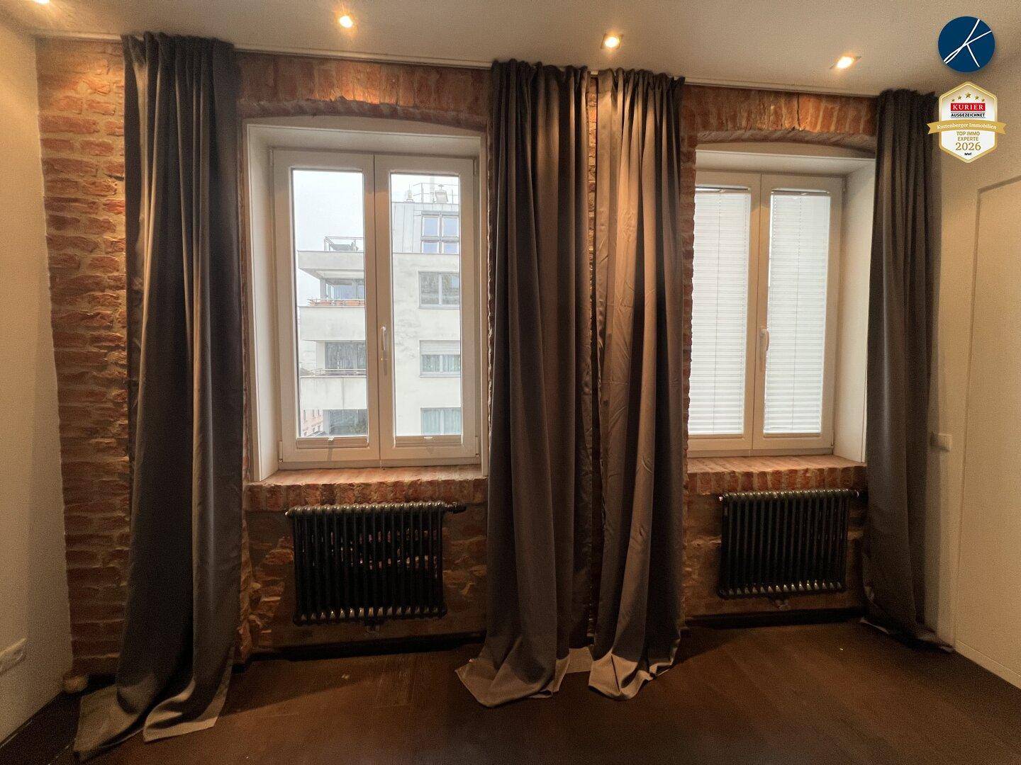 Fensterfront mit dunklen Vorhängen und freiliegenden Ziegelwänden in einem hellen Raum.