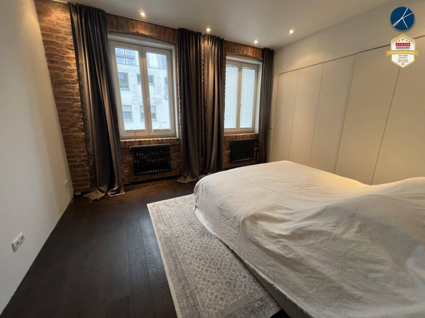Schlafzimmer mit großem Bett, freiliegenden Ziegelwänden und integrierten Kleiderschränken.