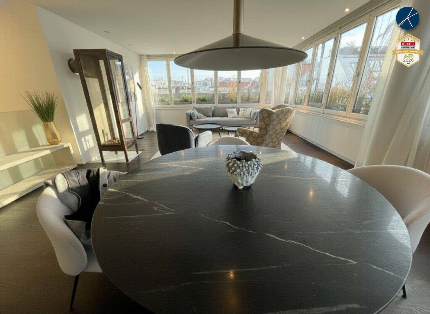 Eleganter Essbereich mit modernem Tisch und Stühlen, dahinter ein heller Wohnbereich mit Stadtblick.